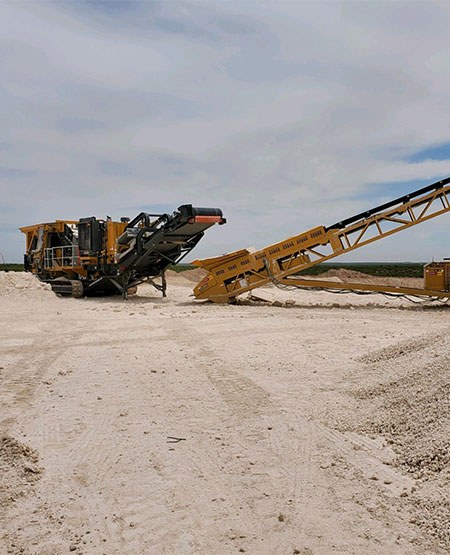 Large crusher service machine from 3G construction in a large white dirt field.