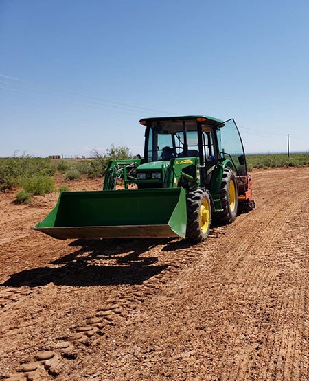 Large green tractor working in a dirt field.