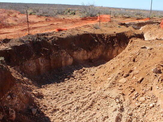 Large dirt pit with orange safety fencing around it.