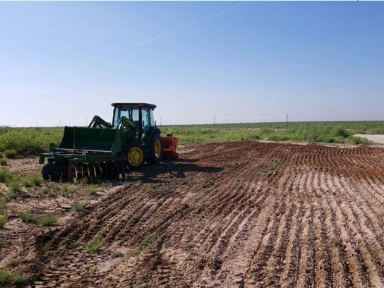 A large green tractor next to an open dirt field with clean dirt lines.