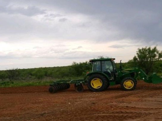 A large green tractor tilling the dirt of an open field.