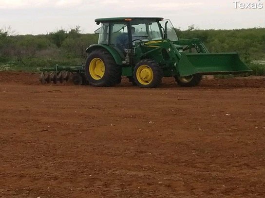 Large green tractor at work in an open dirt field.